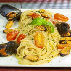 Un piatto invitante di spaghetti con le cozze e pomodorini, guarnito con basilico fresco.