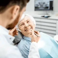 Un dentista esamina i denti di un'anziana sorridente, sottolineando l'importanza dell'igiene orale per gli anziani.