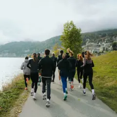 Grupa biegaczy w malowniczej scenerii nad jeziorem. Widok z tyłu na ludzi w sportowych strojach, którzy biegną ścieżką. To inspiracja, jak polubić bieganie.