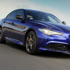 Błękitne Alfa Romeo Giulia Veloce pędzi po drodze, błyszcząc w słońcu.