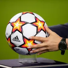 Dłoń z zegarkiem trzyma piłkę Adidas z gwiazdami, gotową do gry w ulubionym klubie piłkarskim na boisku.
