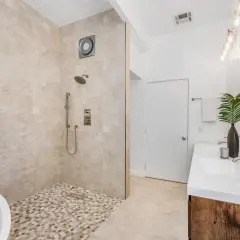 Une salle de bain moderne avec une baignoire îlot, une douche à l'italienne aux galets et un double lavabo. Un exemple de les plus belles douches à l'italienne.