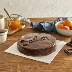 Una deliziosa torta Sacher, lucida e ricoperta di cioccolato, pronta per essere gustata con caffè, albicocche e cioccolato fondente.