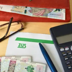 Na stole leżą dokumenty ZUS, pieniądze, kalkulator i okulary. Przygotowanie do złożenia wniosku o świadczenie wspierające.