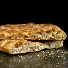 Schiacciata toscana dorata e fragrante, tagliata a metà, con alveolatura evidente e briciole sparse.