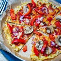 Vegane blumenkohl pizza mit Paprika, Zwiebeln und Pilzen, auf Backpapier serviert.