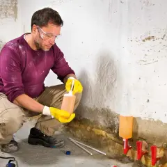Mann mit Schutzbrille und Handschuhen behandelt feuchte Wand mit Injektionsflüssigkeit. So wird die Wand trocken.