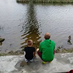 Dwóch chłopców obserwuje kaczki na brzegu jeziora Kisajno.