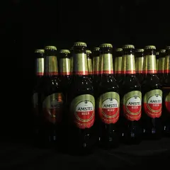 Rząd butelek piwa Amstel na czarnym tle. Zastanawiasz się, jakie piwo kraftowe wybrać? Amstel to klasyka.
