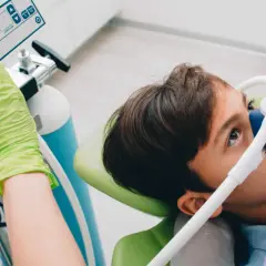 Chłopiec z maską na twarzy, dentysta reguluje aparat. To nie jest głupi jaś, tylko profesjonalny sprzęt do sedacji.