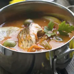 Aromaticzna rosyjska zupa rybna z kawałkami ryby, oliwkami, cytryną i natką pietruszki w metalowej misce.