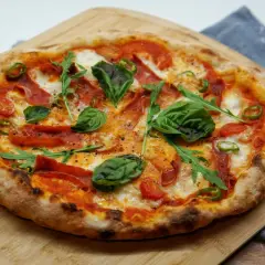 Pizza maison avec une pâte à pizza préparée la veille, garnie de tomates, mozzarella, roquette, basilic, piments et salami.