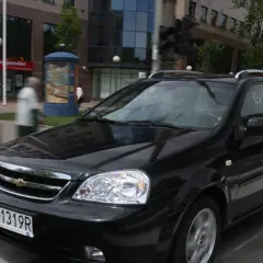 Czarny Chevrolet Lacetti kombi jedzie ulicą, mijając budynki i przechodniów.