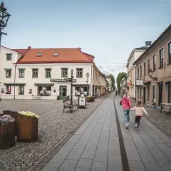 Två flickor springer glatt längs en kullerstensgata i Vadstena. Besök Vadstena för en charmig upplevelse.