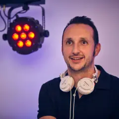 DJ mit Kopfhörern bereit für die Party in Bergisch Gladbach. Scheinwerfer leuchten im Hintergrund.