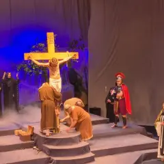 Scena ukrzyżowania Jezusa, odtworzenie biblijnego misterium. Wokół krzyża zgromadzeni ludzie w historycznych strojach, żołnierze rzymscy i kobiety.