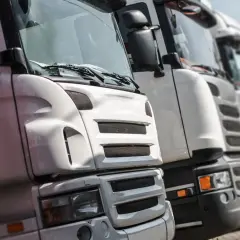 Rząd białych ciężarówek, każda imponująca swoją wielkością. Trudno ocenić, ile wysokosci ma ciezarowka, ale na pewno są to potężne maszyny.