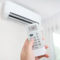 Mano sujetando control remoto de aire acondicionado, ajustando el símbolo frío a 19°C para un ambiente fresco.