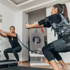 Kobiety w kamizelkach EMS wykonują przysiady. Trening z elektrostymulacją mięśni (EMS) to przyszłość fitnessu.