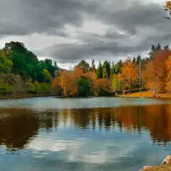 Reflejos otoñales en el lago Castiñeiras, con árboles de colores vibrantes y un cielo nublado.
