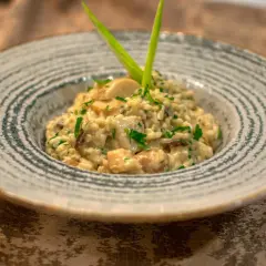 Kremowe risotto ze szparagami i grzybami, udekorowane zieloną cebulką i natką pietruszki, podane w ozdobnej misce.