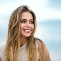 Lachendes junges Mädchen mit langen, welligen Haaren, die blonde Highlights auf dunkelblond zeigen.