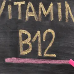 Kreidezeichnung "VITAMIN B12" auf einer Tafel, daneben eine Hand mit pinker Kreide.