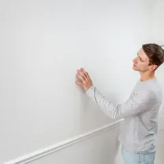 Man känner på en vit vägg, redo att ta bort tapet för att fräscha upp rummet.