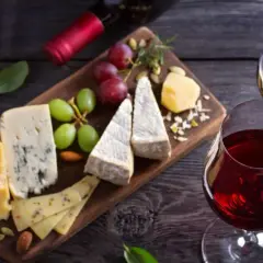 Un tagliere di formaggi misti, uva e frutta secca, perfetto per i rosso di Montalcino abbinamenti. Due calici di vino rosso completano la scena.