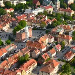 Urokliwe zabytkowe miasto nad Wisłą, z Rynkiem i wieżą ratuszową, otoczone kamienicami z czerwonymi dachami.