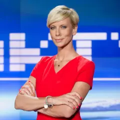 Małgorzata Łaszcz, dziennikarka, w czerwonej sukience, z krótkimi blond włosami, na tle studia TVN.