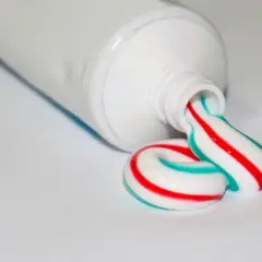 Kolorowe paski na paście do zębów, czerwone i turkusowe, tworzą spiralę wychodzącą z tubki.