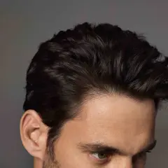 Primer plano de un hombre con mas cantidad de pelo oscuro y peinado hacia atrás, mostrando su oreja y parte de su rostro.