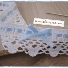 Delicati pizzi all'uncinetto lavorati su stoffa, rifiniti con nastrini azzurri e un fiocco.