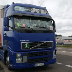 Niebieski Volvo FH Globetrotter z naczepą, zaparkowany przy drodze. W tle sklep i inne ciężarówki. Zakazy dla ciężarówek 40ton.