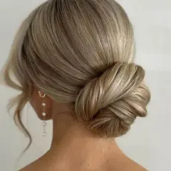 Elegante Hochzeitsfrisur mit einem kunstvoll gedrehten Dutt und zarten Perlenohrringen. Perfekt für den großen Tag.