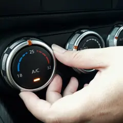 Dłoń reguluje pokrętłem temperaturę klimatyzacji w samochodzie, ustawiając ją na 25 stopni.
