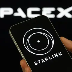 Dłoń trzyma smartfon z logo Starlink na ekranie, w tle logo SpaceX.