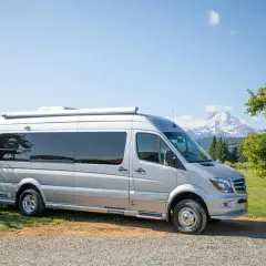 Srebrny, używany camper stoi na tle gór i sadu. Gotowy na przygodę!