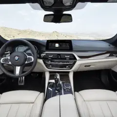Wnętrze BMW 5 G30 z jasną tapicerką, drewnianymi wstawkami i nowoczesnym ekranem multimedialnym.