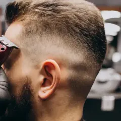 Barbero con guantes negros crea un corte de pelo **low fade** a un hombre con una máquina.