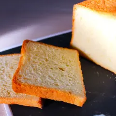 Pain de mie moelleux, parfait pour une recette pain de mie boulangerie maison. Deux tranches dorées et un pain entier sur un plateau sombre.