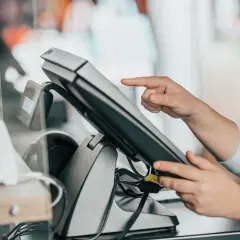 Dłoń dotyka ekranu terminala płatniczego. To jest właśnie point of sale, czyli miejsce sprzedaży.
