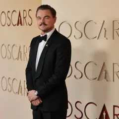 Leonardo DiCaprio w eleganckim smokingu pozuje na tle ścianki z napisem "OSCARS".