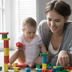 Uśmiechnięta mama bawi się klockami z dzieckiem. Zastanawiasz się, ile kosztuje opieka nad dzieckiem?
