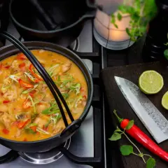 En väldoftande thaigryta med kyckling, toppad med chili och salladslök. Bredvid ligger en kniv, lime och chili.