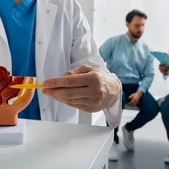 Lekarz omawia z pacjentem model układu moczowo-płciowego, wskazując na obszar prostaty. Rozmowa dotyczy potencjalnych objawów raka prostaty.