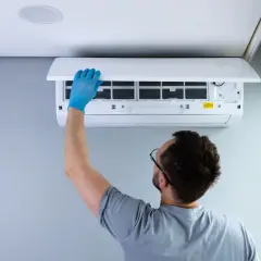 Hombre con guantes azules revisa filtros de aire acondicionado. Se acabó el ruido molesto.