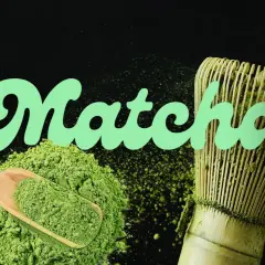 Poudre de matcha verte, cuillère en bois, fouet et tasse de boisson, évoquant le goût matcha authentique.