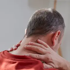 Mężczyzna masuje kark, szukając ulgi w bólu. Czy to początek problemu, jak zlikwidować wdowi garb?